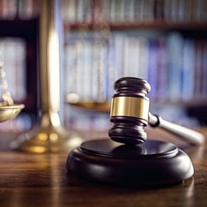A judge's gavel and scales of justice on a wooden table in a library - Leep Tescher Helfman and Zanze