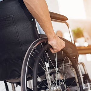 Hand grips wheelchair wheel, person in black, indoor setting, bone pain. - Leep Tescher Helfman and Zanze