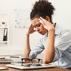 Woman at desk holding neck in discomfort, laptop, notepad, and glasses nearby, illustrating workplace injury - Leep Tescher Helfman and Zanze