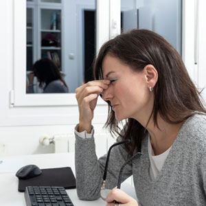 A woman sitting on a table hand on eyes - Work-Related Eye Injuries