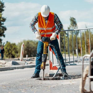 Worker using drill to dig hole in ground at construction site. - Leep Tescher Helfman and Zanze