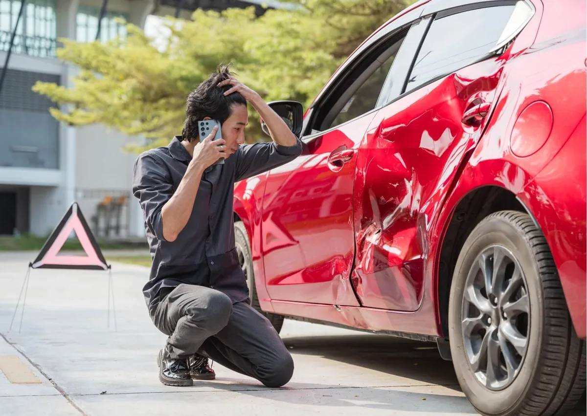Driver inspecting damage to a personal vehicle after an accident while driving for work, illustrating a potential workers' compensation claim.