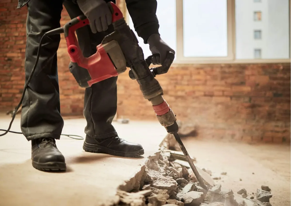 Construction worker using a jackhammer to break concrete, illustrating dust exposure risks that may support a workers' compensation claim for building-site dust injuries.