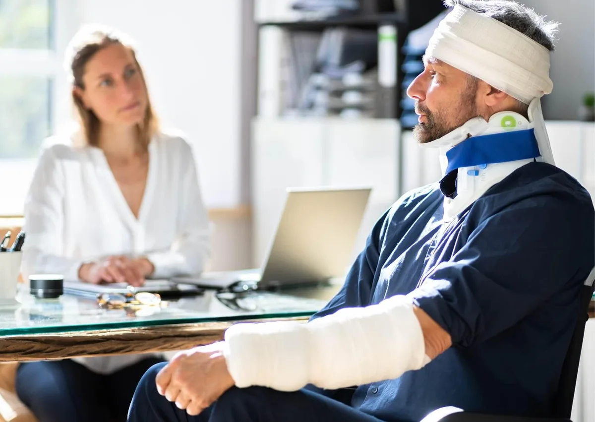 Injured construction worker wearing a neck brace and arm cast meeting with a roofing injury lawyer to discuss a workplace accident claim.