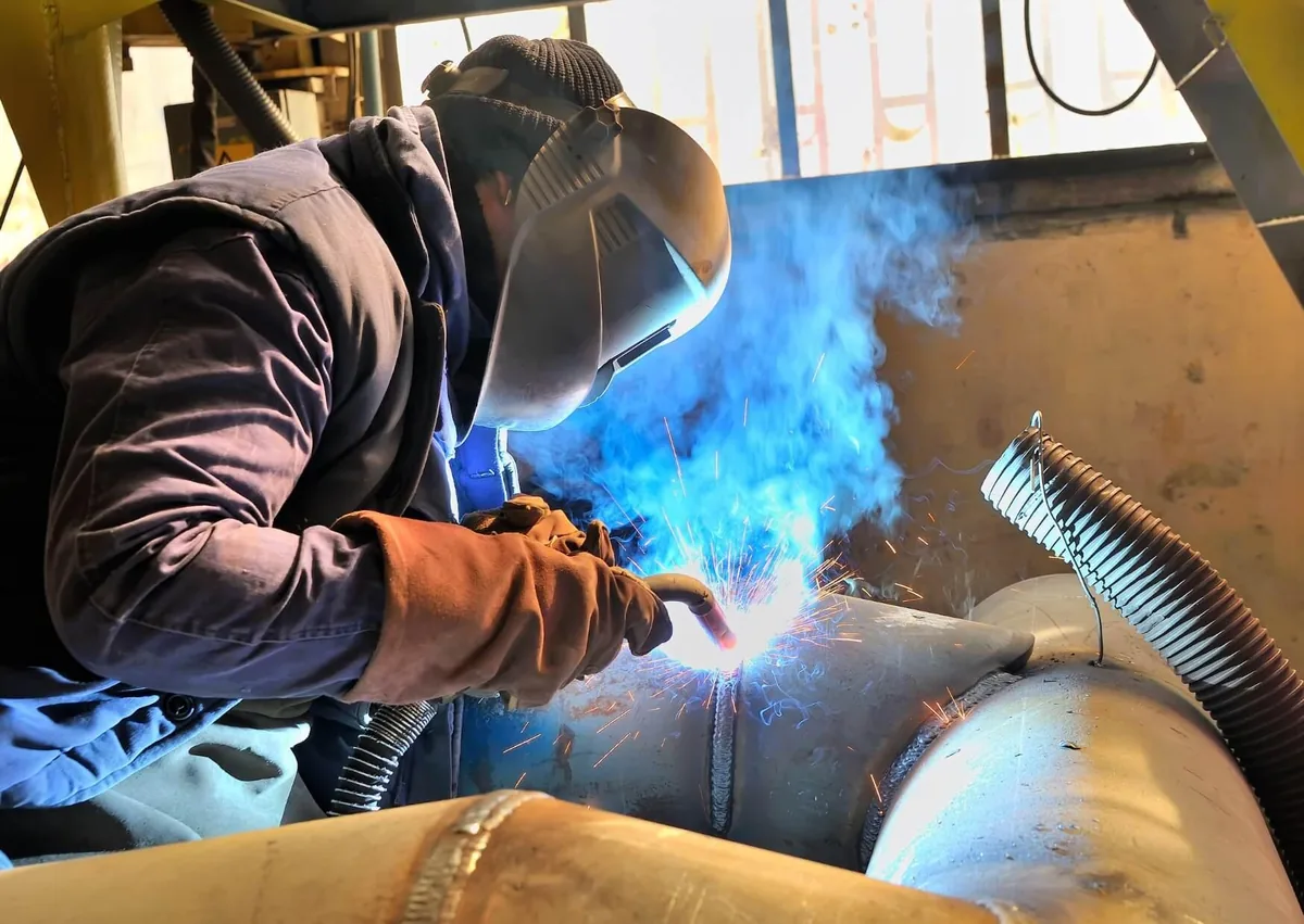 Industrial worker welding large metal pipes while wearing protective gear, illustrating a workplace accident case for a welding accident lawyer.