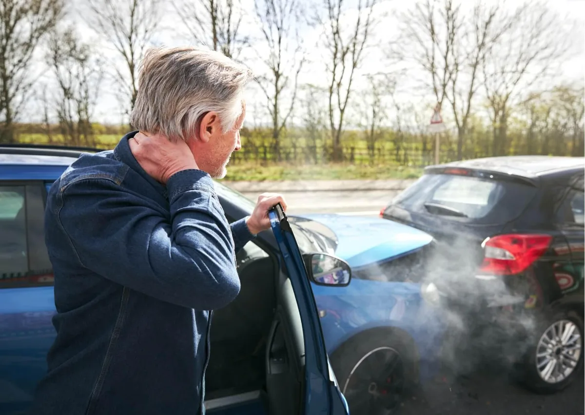 Driver holding their neck after a work-related car accident beside two damaged vehicles, illustrating a potential workers' compensation injury claim.