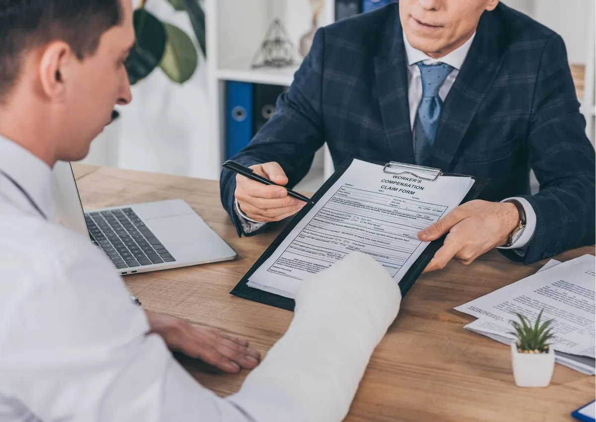 Worker with an arm injury reviewing workers' comp nerve damage settlement paperwork with an attorney during a claim consultation.